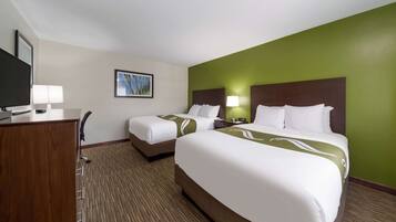 A hotel room with two beds, a desk with a lamp, a television, and a framed picture on the wall.