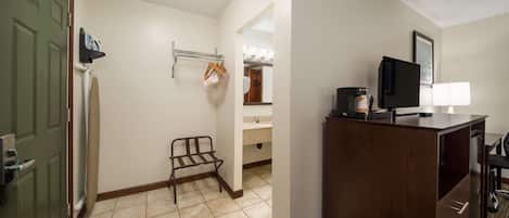 A hotel room with a wooden desk, a television, a mirror, and a bathroom visible through an open door.