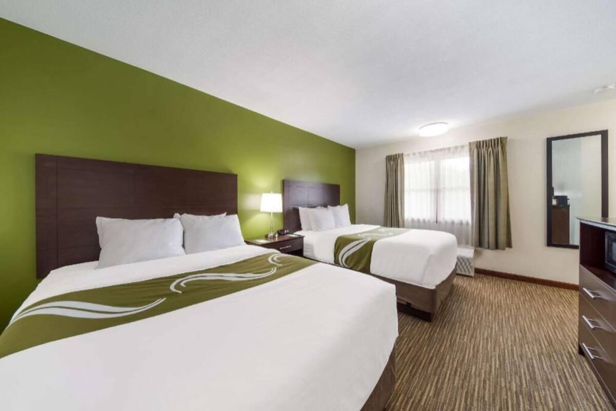 Ein Hotelzimmer mit zwei Betten, einem großen Spiegel, einem Fernseher und einem Fenster mit Vorhängen.