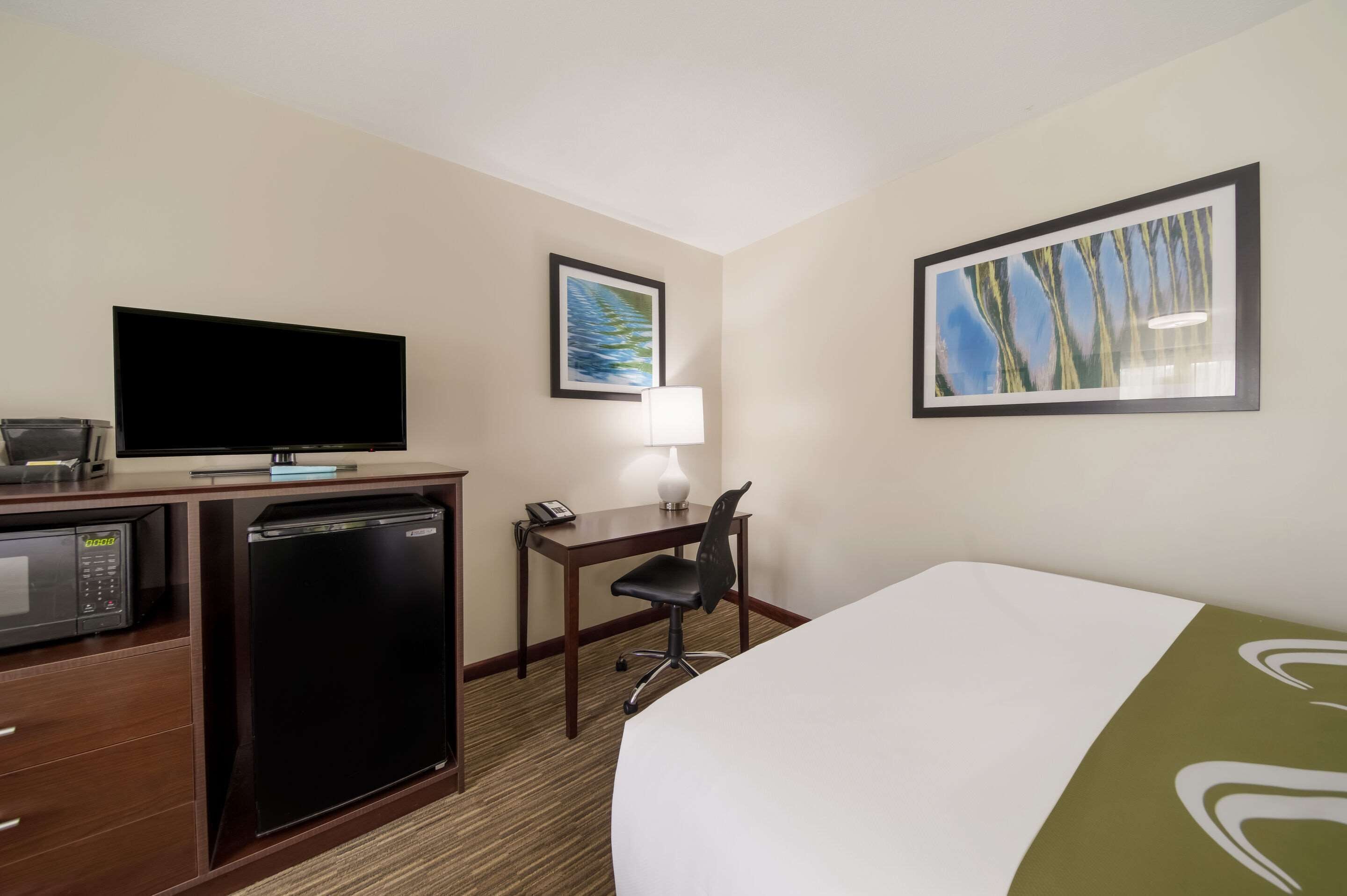 A hotel room with a bed, a desk with a lamp, a television, a mini-fridge, and a microwave.