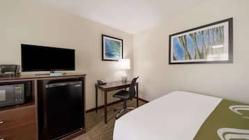 Ein Hotelzimmer mit Bett, Schreibtisch mit Lampe, Fernseher, Minikühlschrank und Mikrowelle.