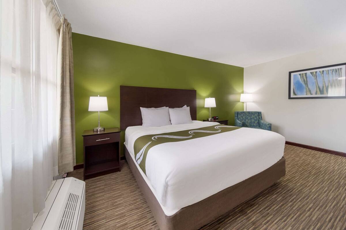 Ein Hotelzimmer mit einem großen Bett, zwei Nachttischen mit Lampen, einem Sessel, einem Gemälde an der Wand und einer Heizung.