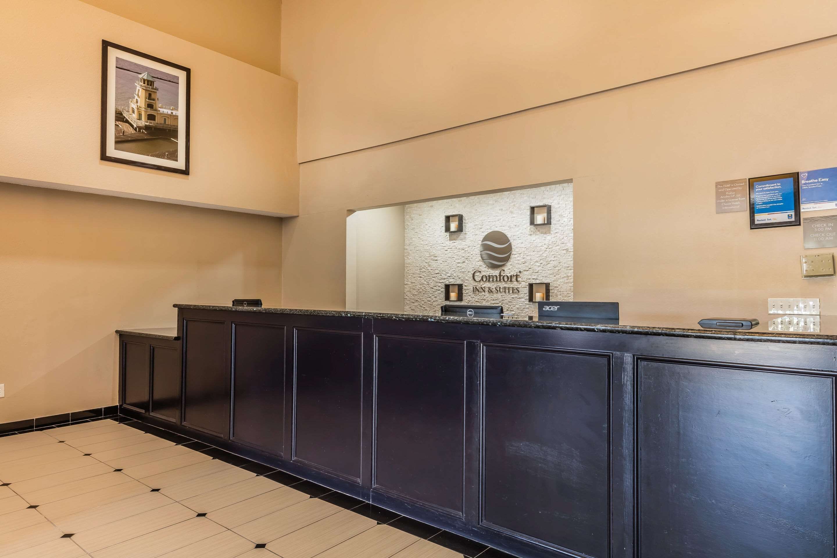 A reception desk with a framed picture above it, a sign for Comfort Inn & Suites, and a digital display.