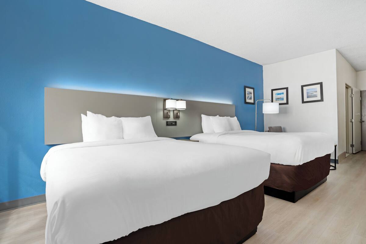A hotel room with two beds, a blue accent wall, and a modern design.