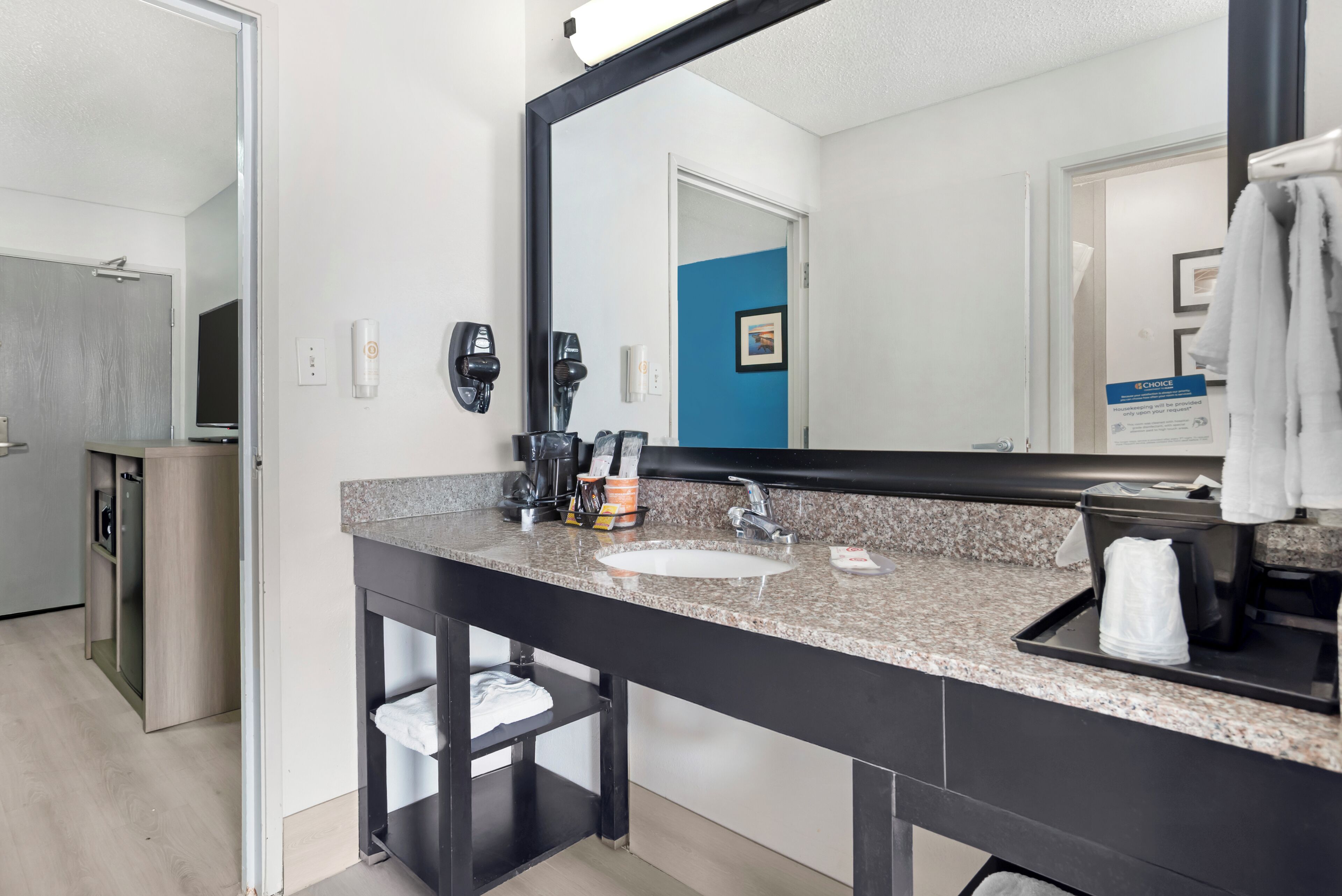 Un baño moderno con encimera de granito, un lavamanos, un espejo grande y un perchero para toallas.