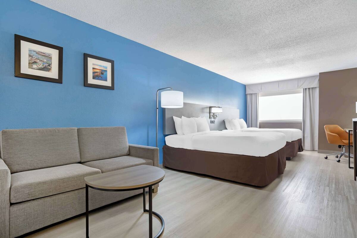 A hotel room with a sofa, a small table, a bed with a headboard, a lamp, and two framed pictures on the wall.