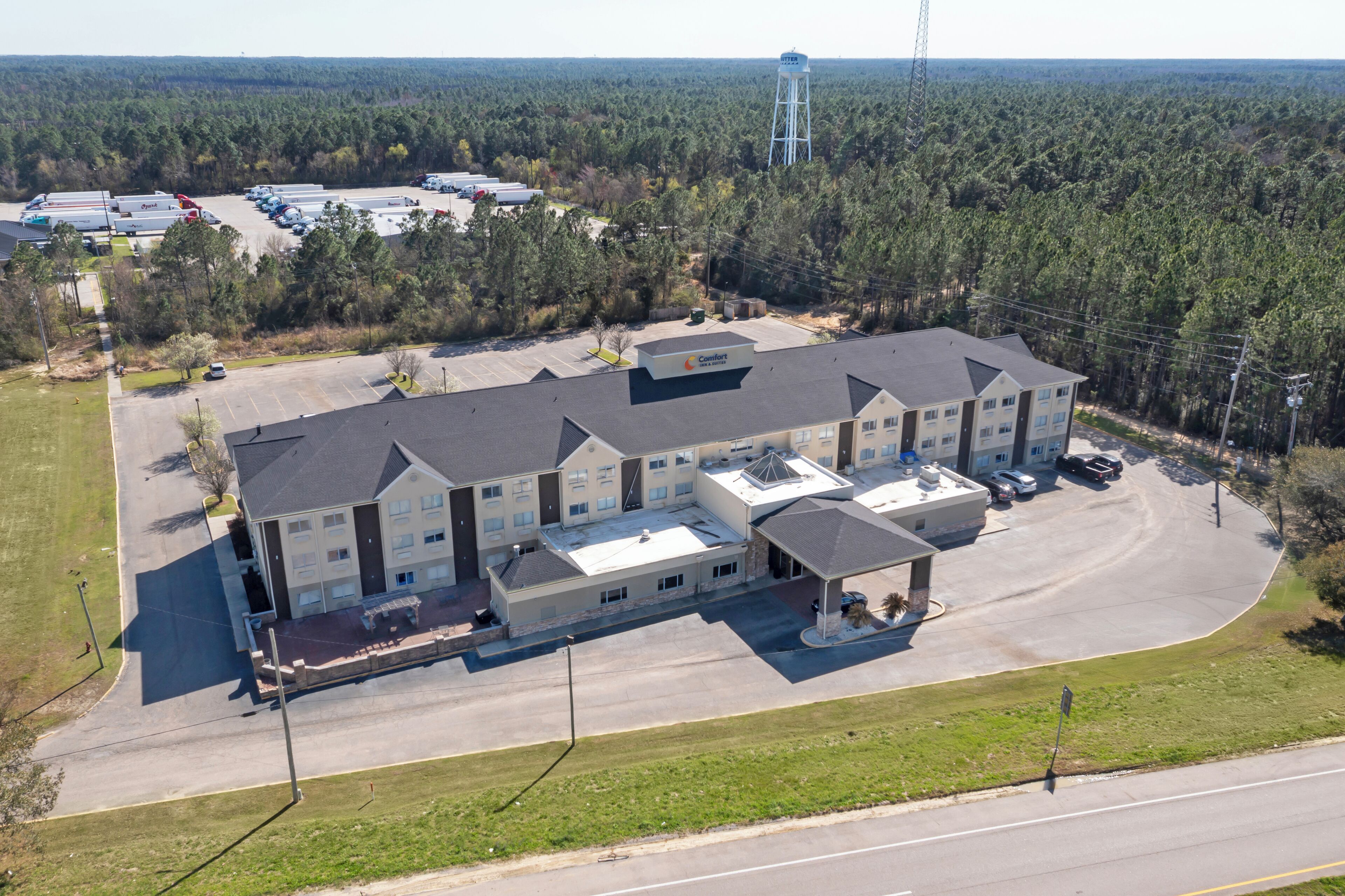 A multi-story hotel with a parking lot, surrounded by trees and a water tower in the distance.