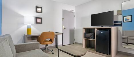 Ein modernes Wohnzimmer mit Sofa, einem kleinen Tisch, einem Sessel, einem Fernseher, einem Kühlschrank und einer Mikrowelle.