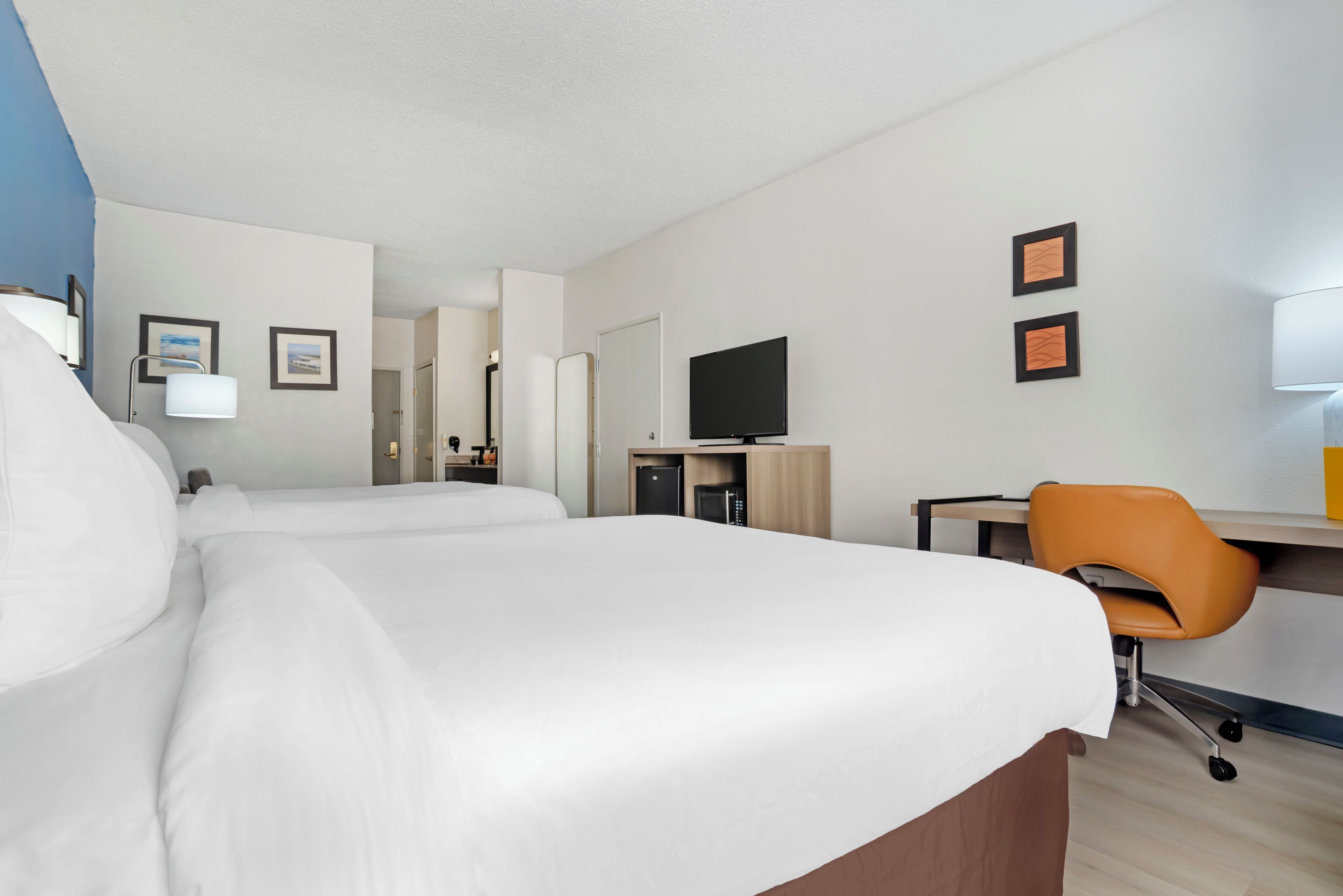 A hotel room with two beds, a desk with a chair, a television, and framed pictures on the wall.