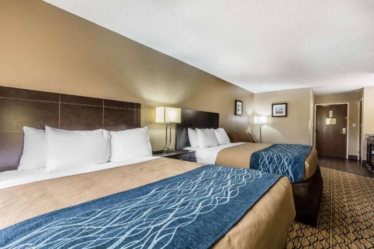 A hotel room with two beds, a headboard, bedside lamps, a desk, and a door.