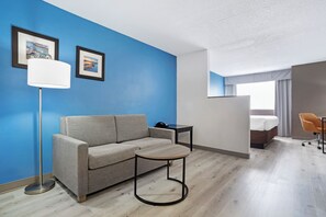 Een moderne hotelkamer met een blauwe accentmuur, een bank, een ronde tafel, een lamp en een bed met uitzicht.