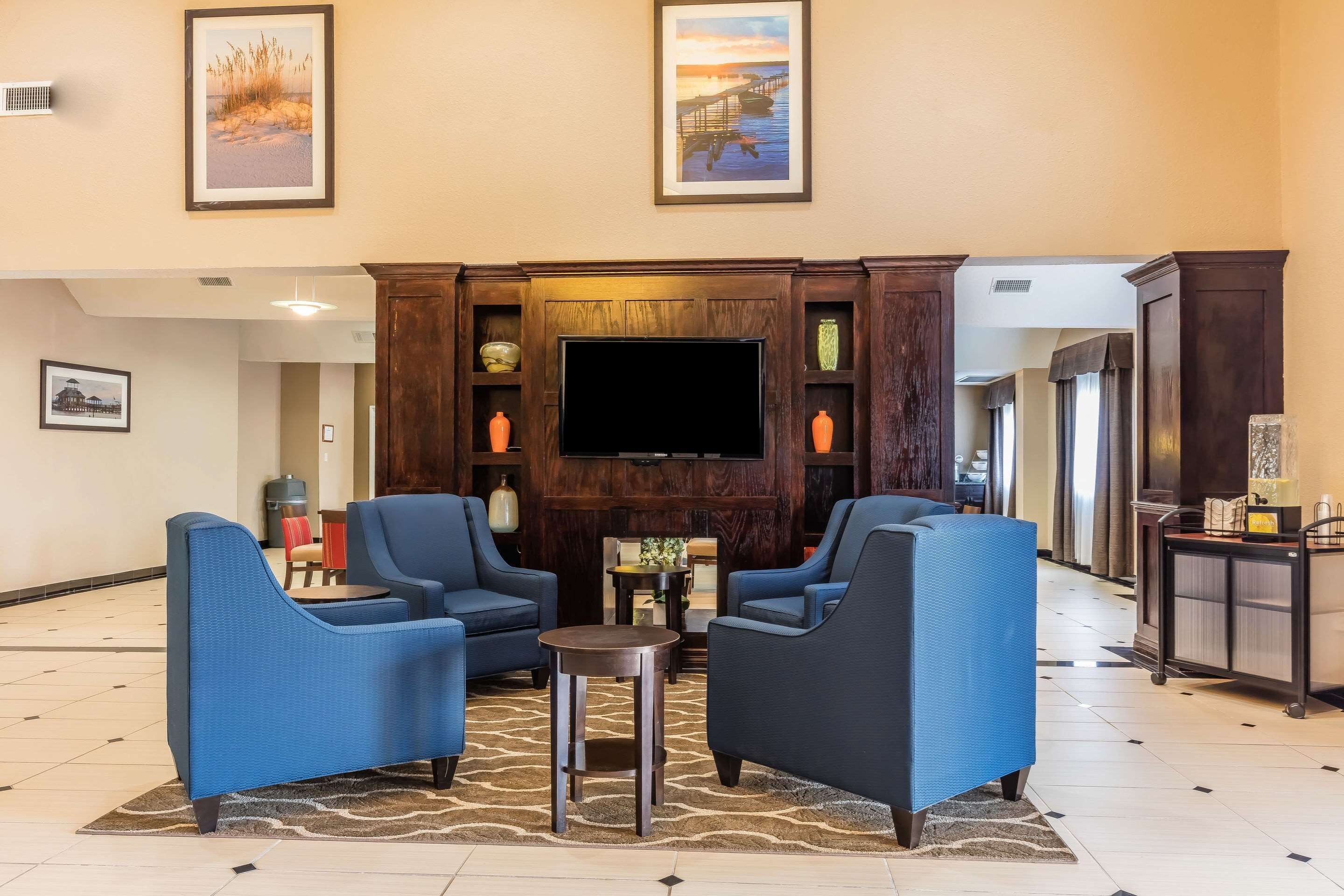 A lobby with blue armchairs, a flat-screen TV, framed artwork, and a reception desk.