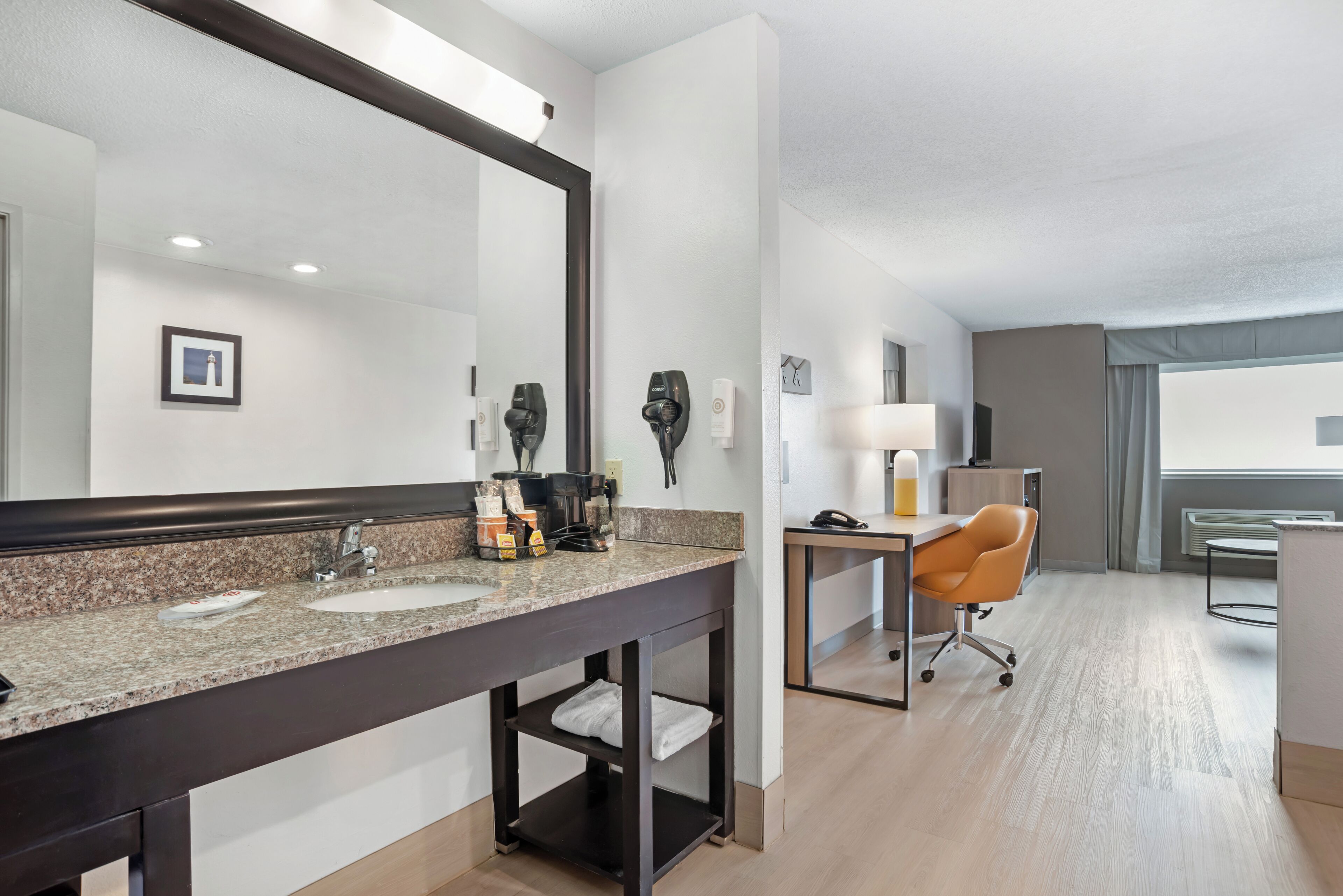 A hotel bathroom with a large mirror, two sinks, a vanity, and a desk with a chair.