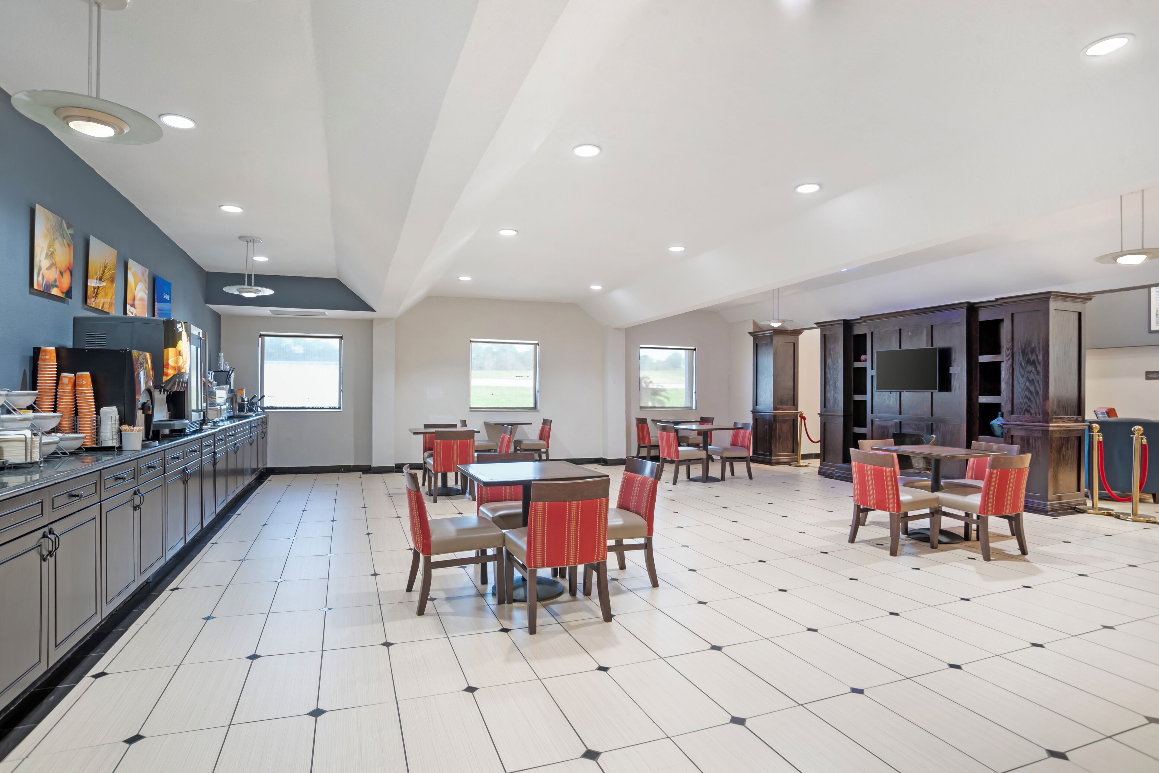 Un vaste espace de salle à manger avec plusieurs tables et chaises, un coin cuisine équipé d’appareils modernes et de grandes fenêtres laissant entrer la lumière naturelle.