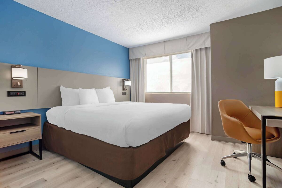 A hotel room with a bed, a desk, a chair, and a window with curtains.