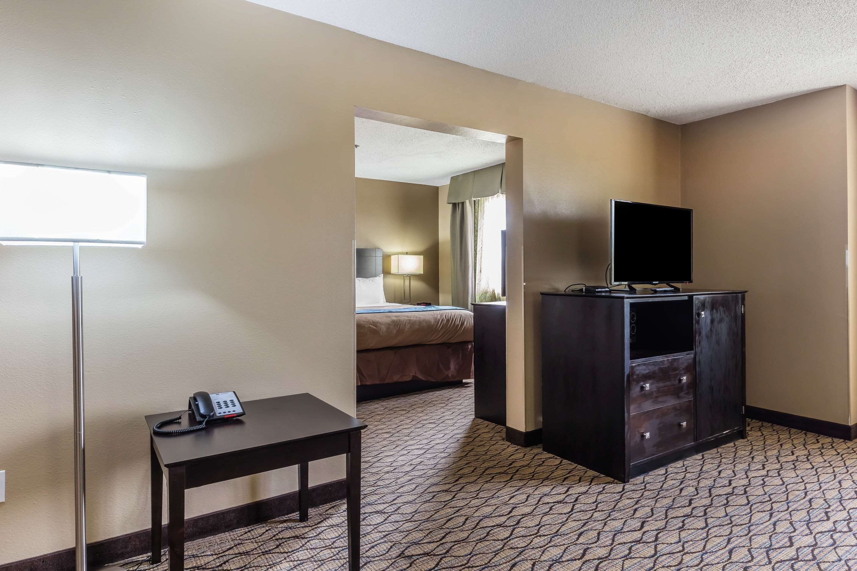 A hotel room with a bed, a desk with a telephone, a television on a cabinet, and a patterned carpet.
