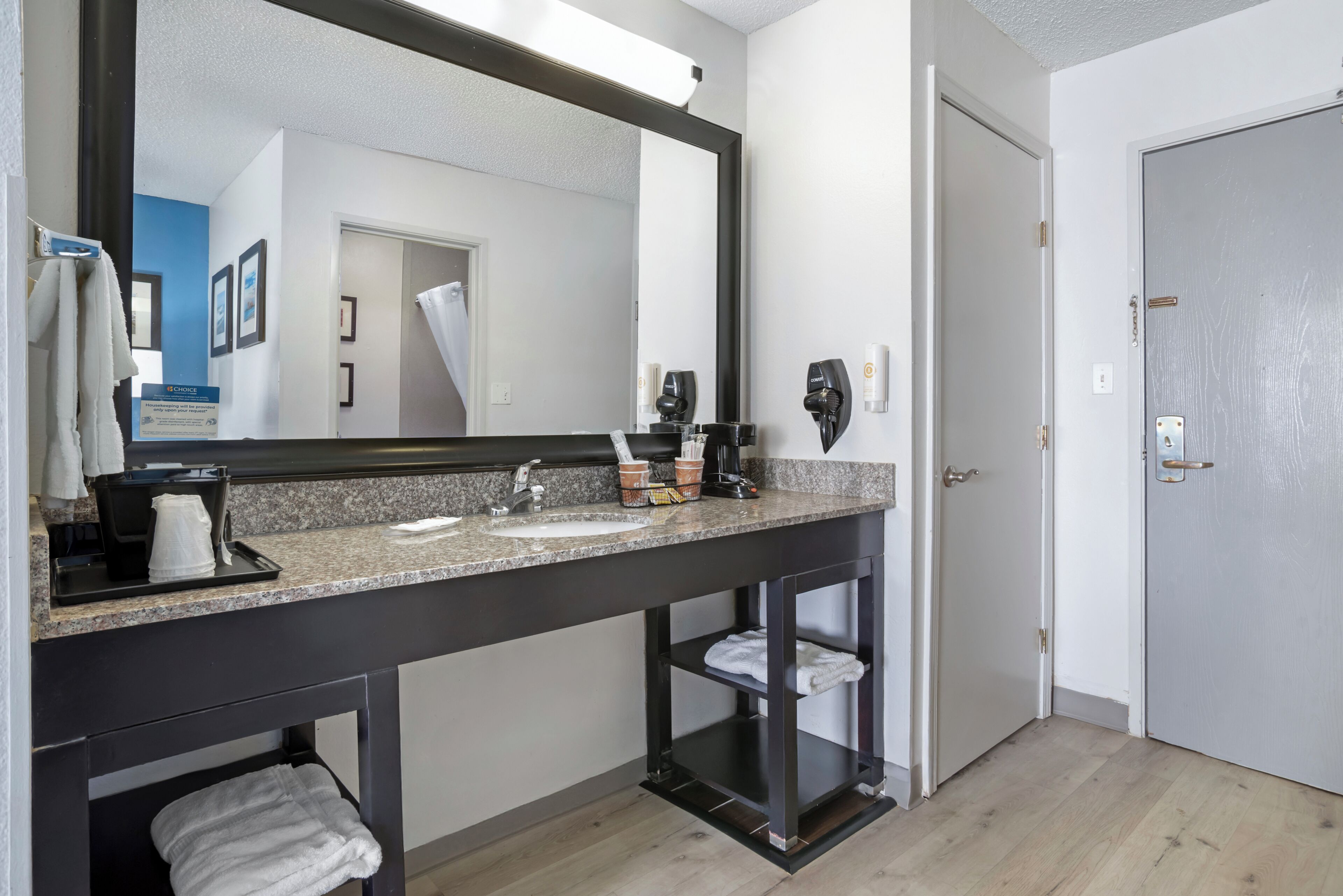 Une salle de bain avec un grand miroir, deux lavabos, un porte-serviettes et une étagère.