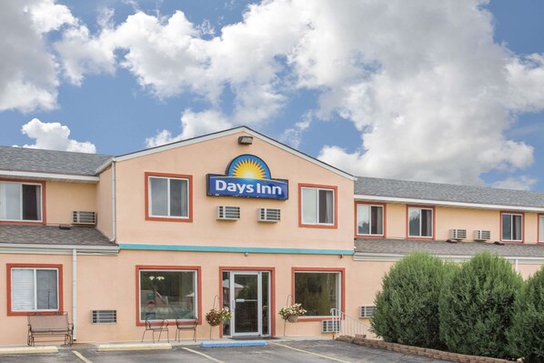 A Days Inn hotel with a peach-colored exterior, multiple windows, and a clear blue sky with clouds.