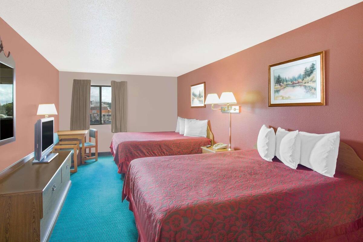 A hotel room with two beds, a desk with a TV, a chair, a desk lamp, a telephone, and a window with curtains.