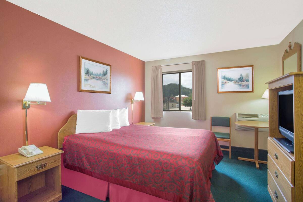 A hotel room with a bed, bedside lamps, a desk with a television, and two framed pictures on the walls.