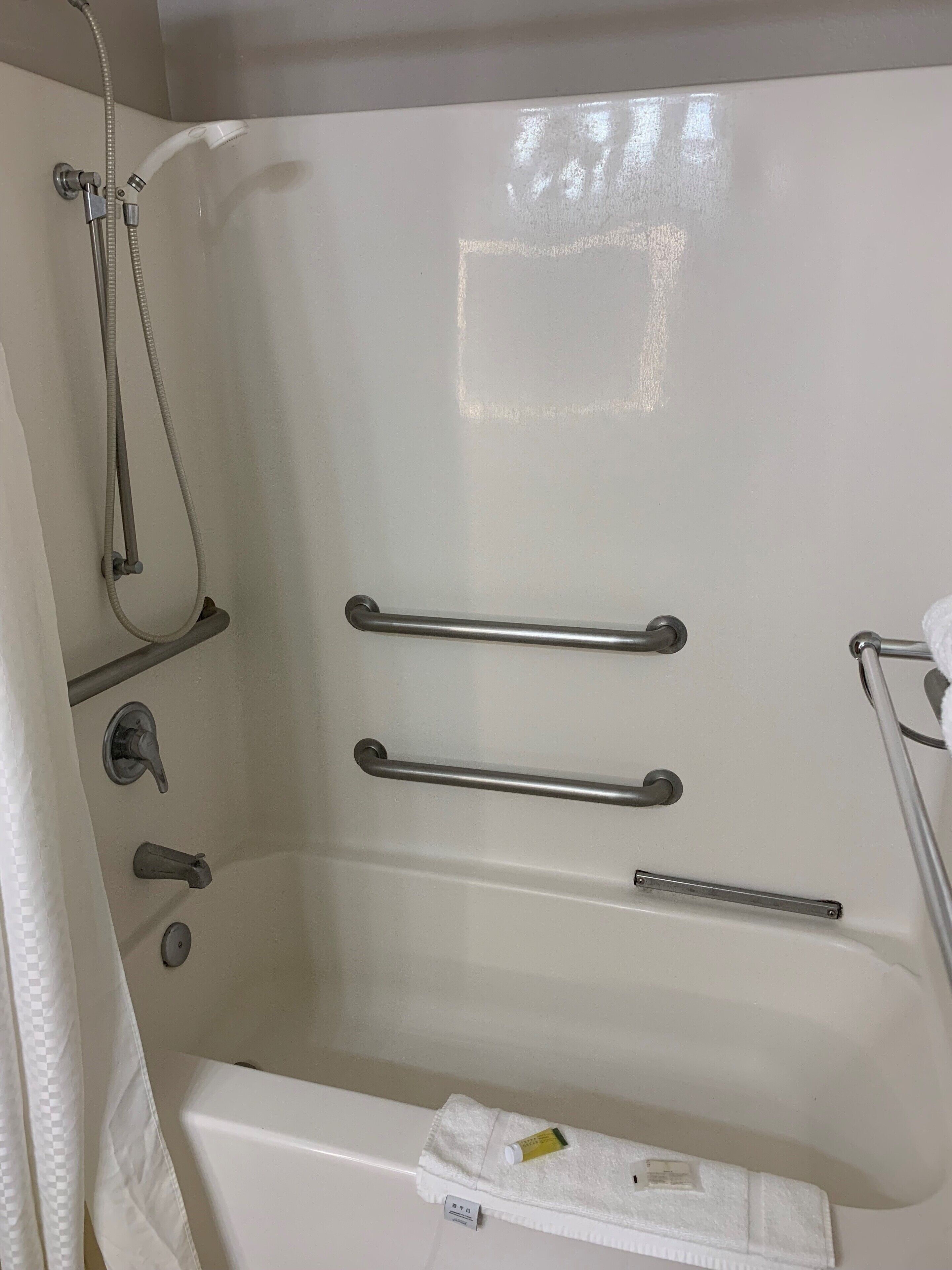 A white bathtub with two grab bars, a showerhead, and a towel rack.