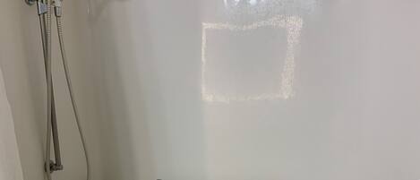 A white bathtub with two grab bars, a showerhead, and a towel rack.
