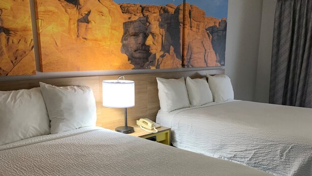 A hotel room with two beds, a nightstand with a lamp and phone, and a large rock painting on the wall. - Days Inn by Wyndham Custer (Custer)