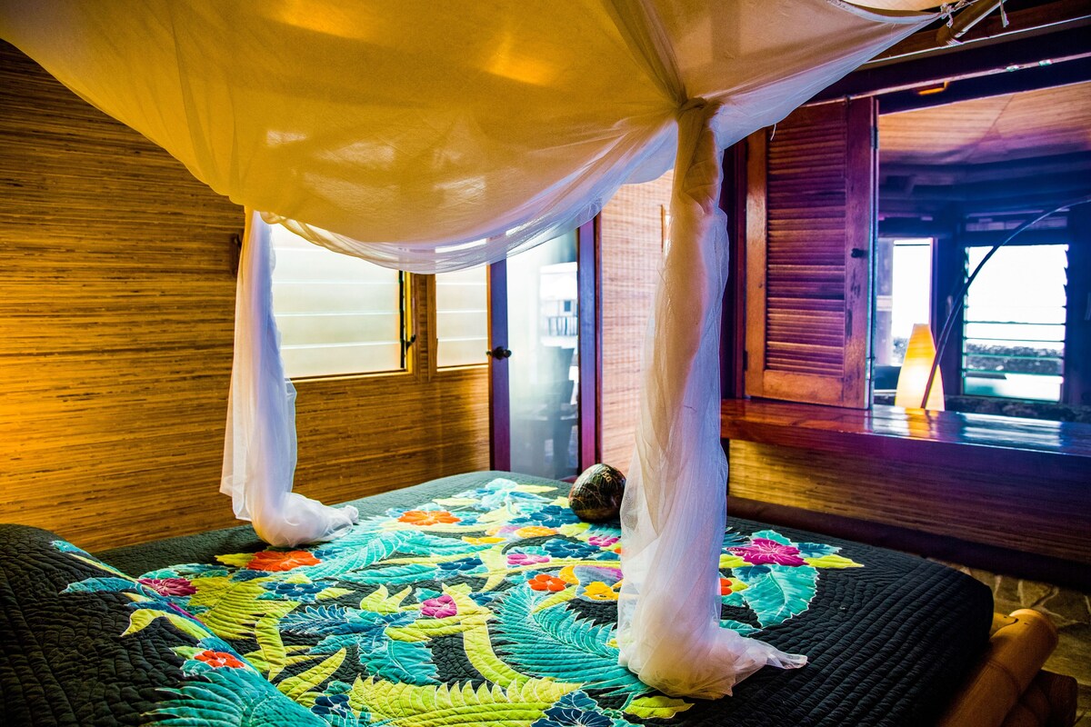 A room with a bed covered in a colorful quilt, a wooden headboard, and a window with a view.