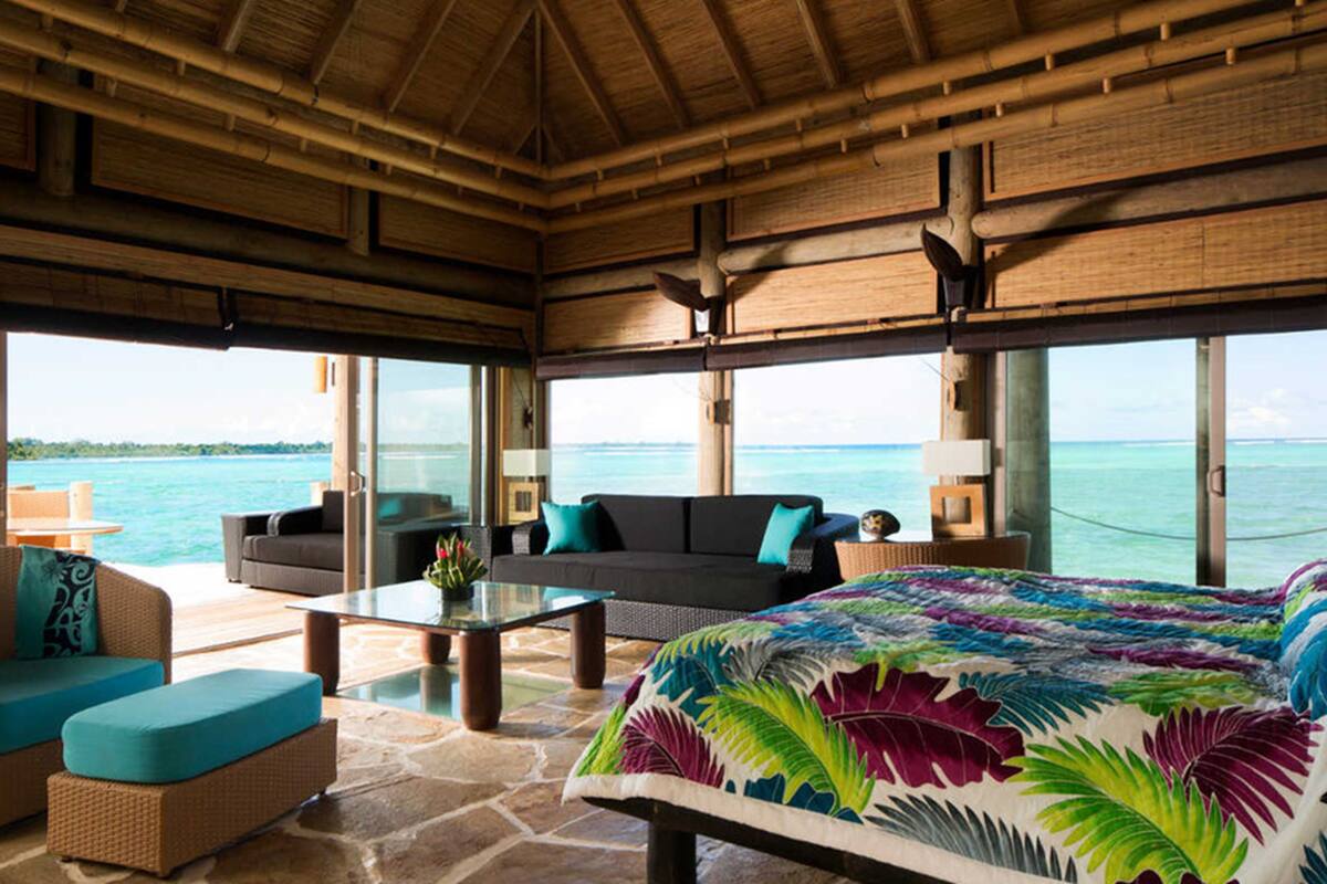 A room with a large bed, a sofa, and a coffee table. There are large windows with a view of the ocean.