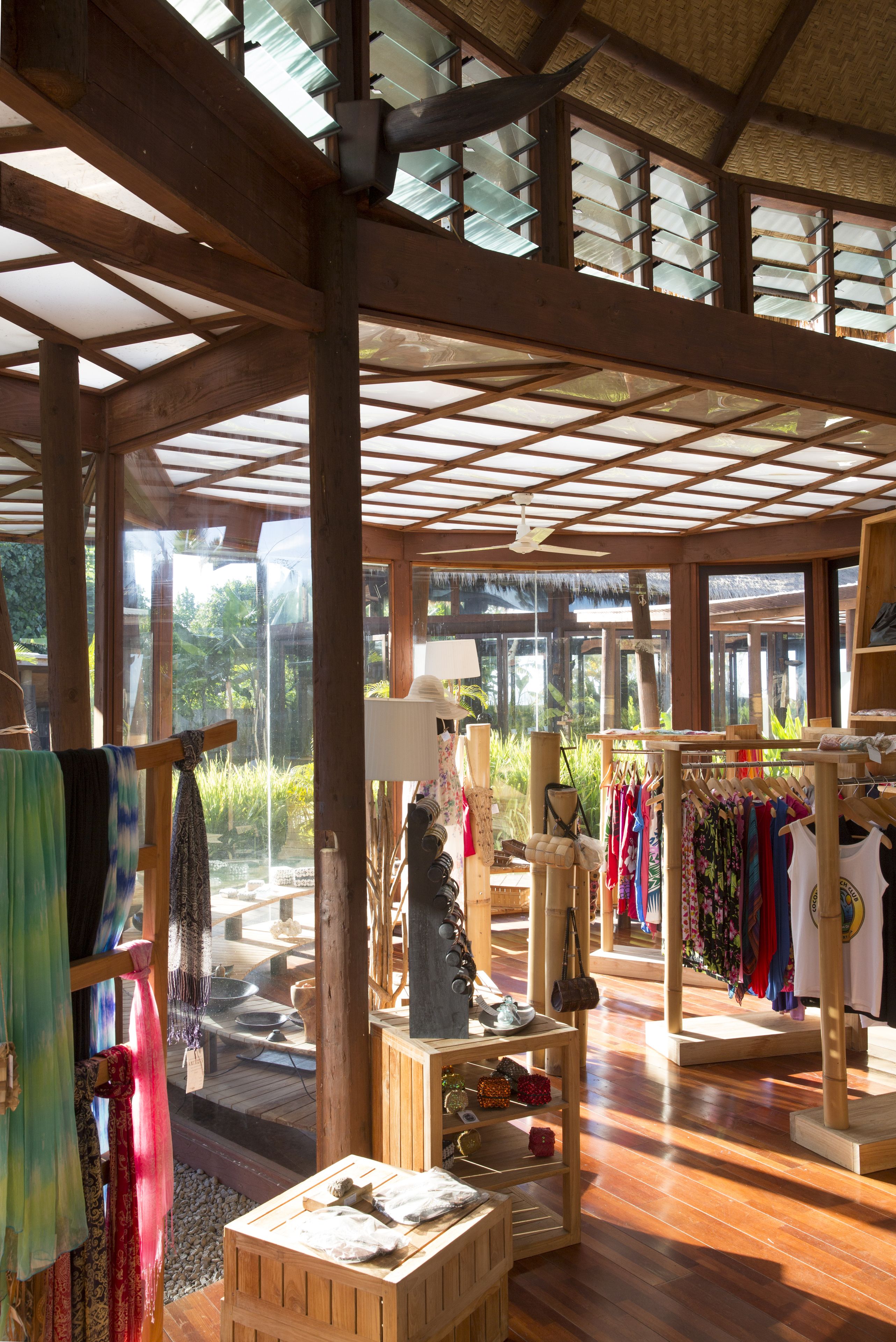 A spacious boutique hotel interior with wooden beams, large windows, and a variety of clothing items displayed on racks.