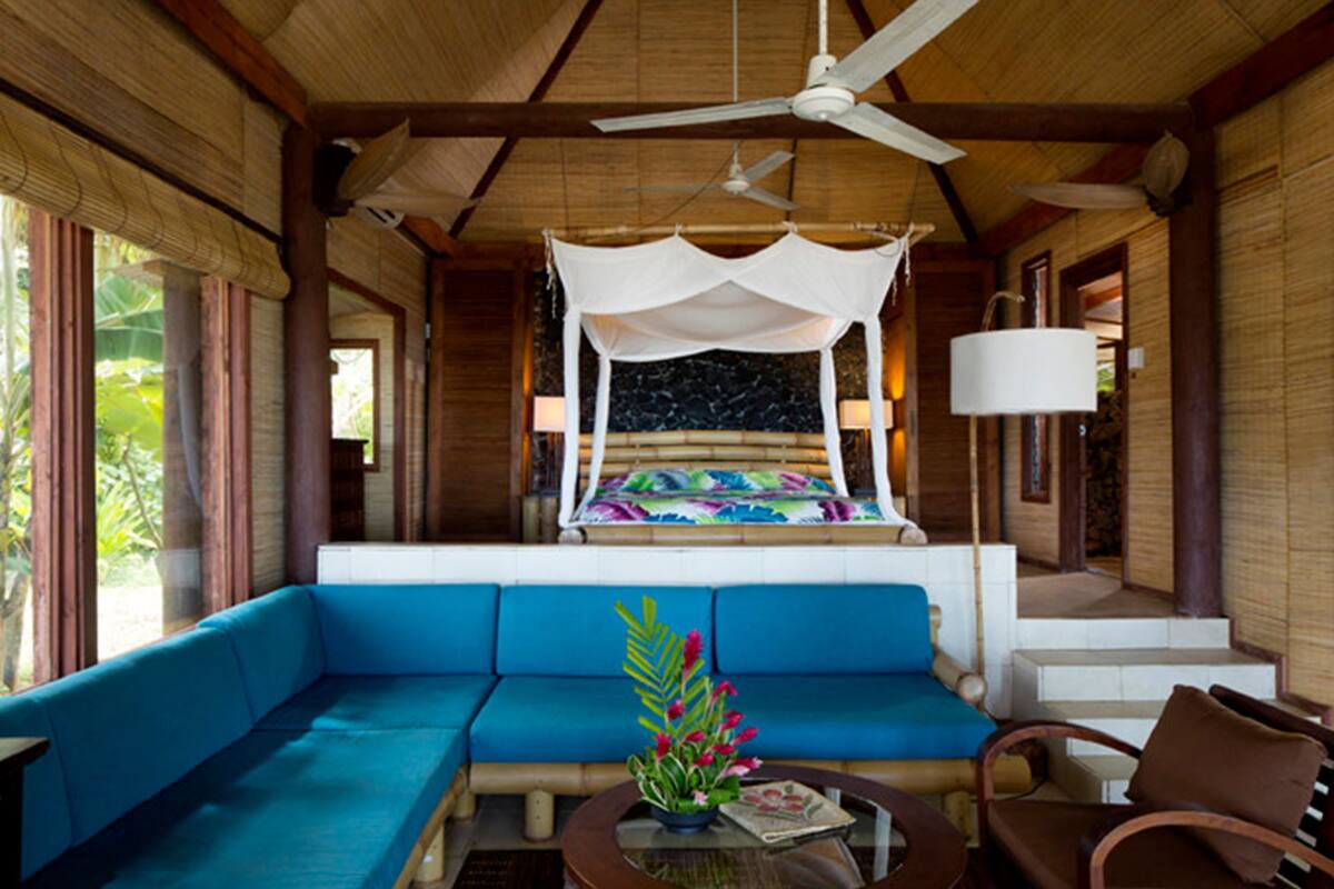 A room with a bed under a canopy, a sofa, a table with a vase, and a ceiling fan.