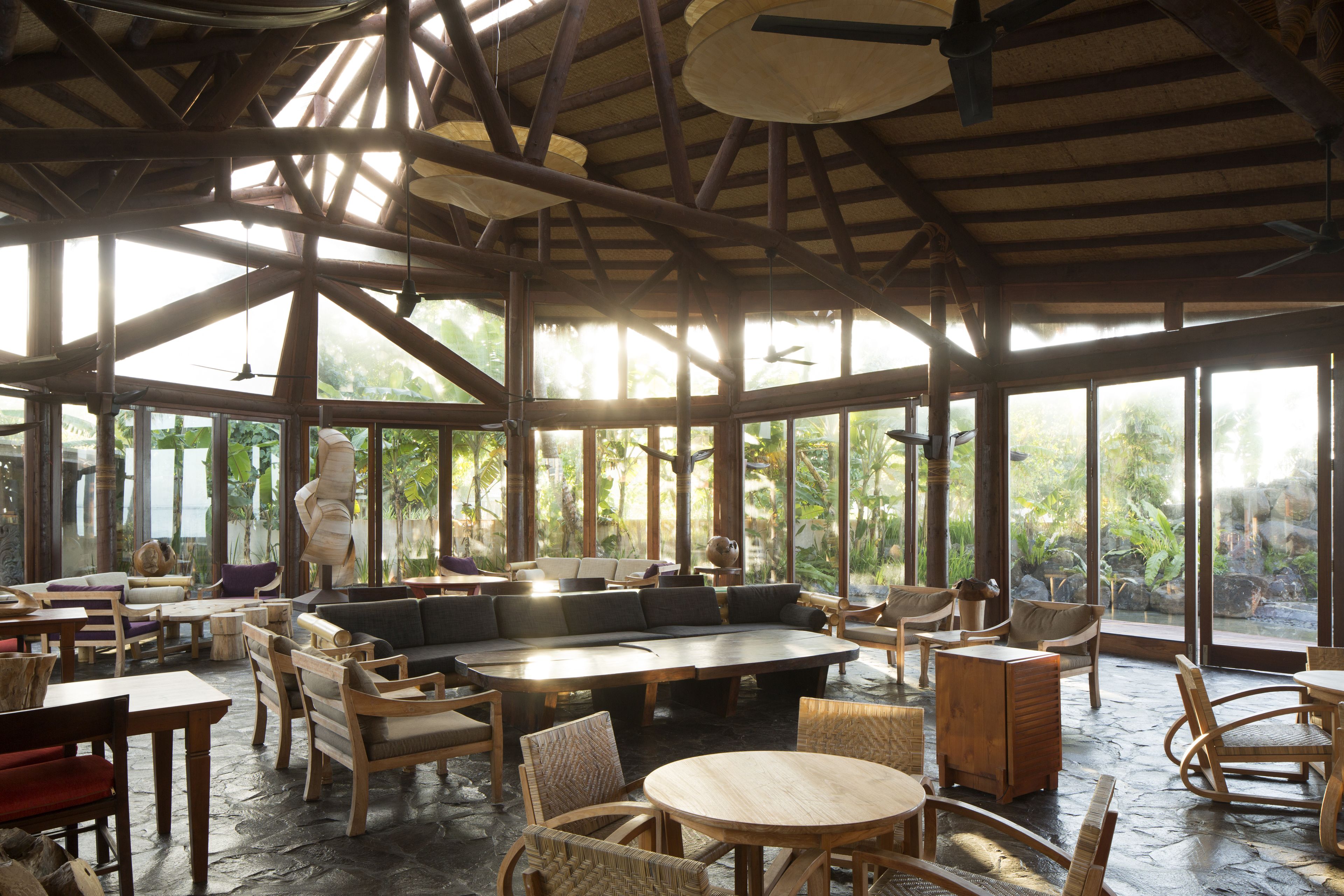A spacious indoor area with wooden furniture, large windows, and a thatched roof.