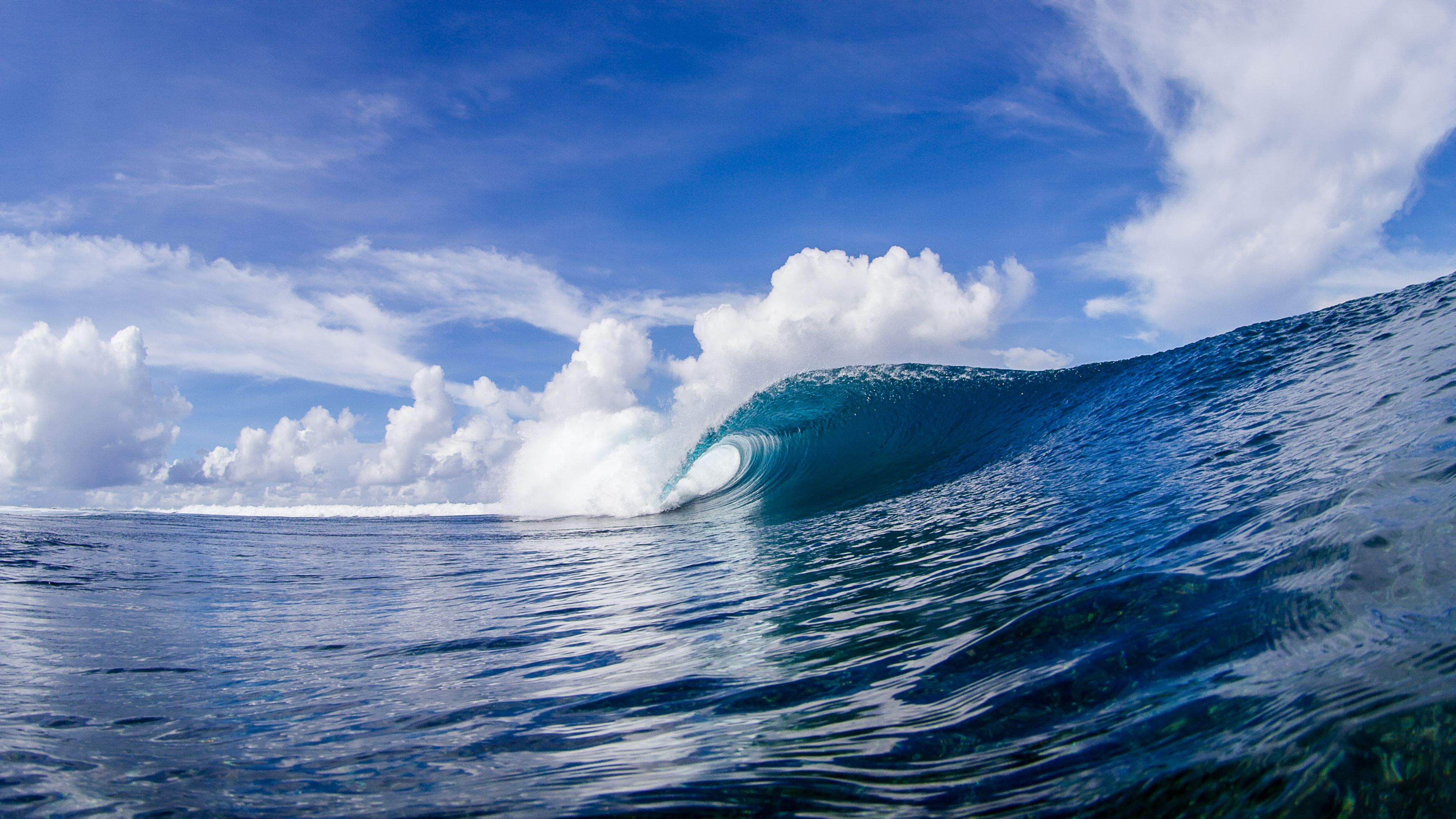 A large wave in the ocean with a clear sky and clouds in the background.