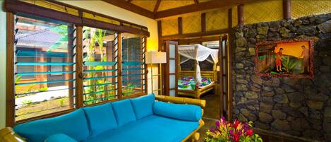 A room with a blue sofa, large windows with horizontal blinds, a stone wall, and a bed with a canopy.