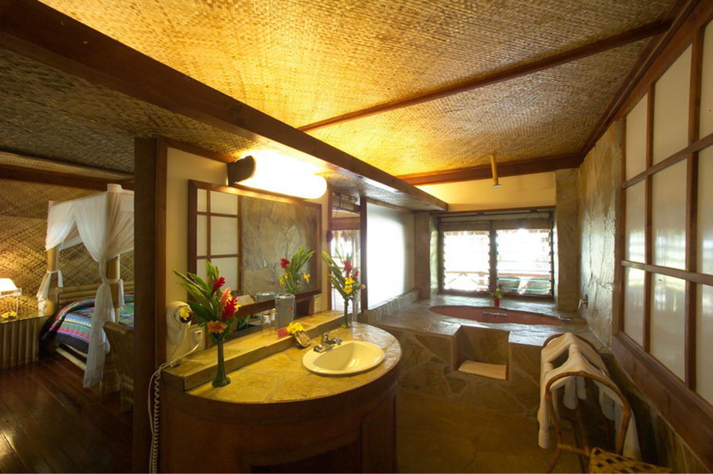 A traditional Japanese-style bathroom with a wooden ceiling, a large mirror, and a sink with a vase of flowers.