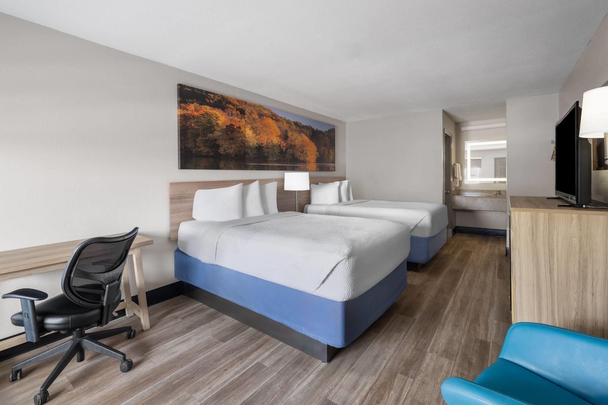 A hotel room with a bed, desk, chair, and a painting of autumn trees.