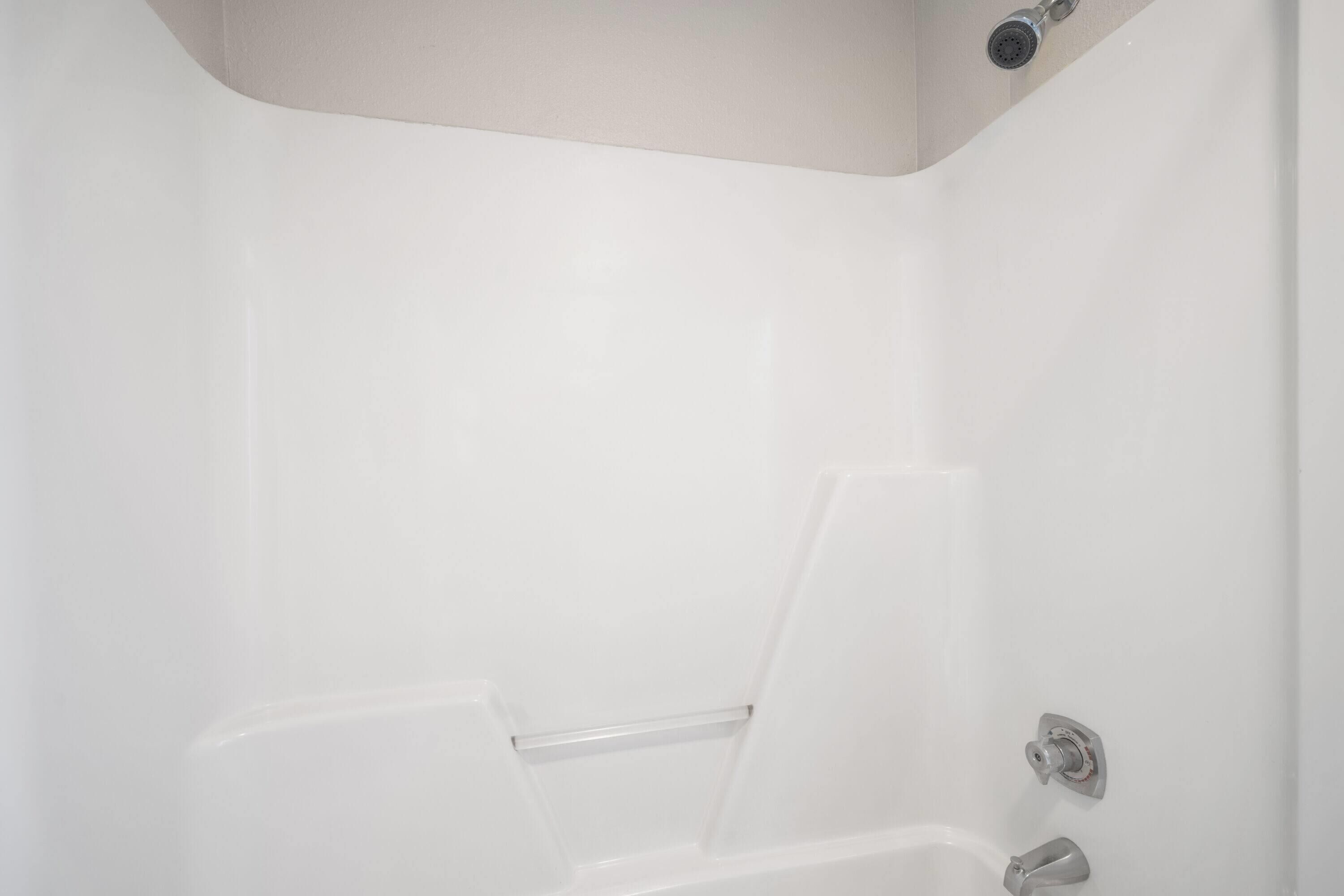 A white, modern bathroom with a shower, a towel rack, and a faucet.
