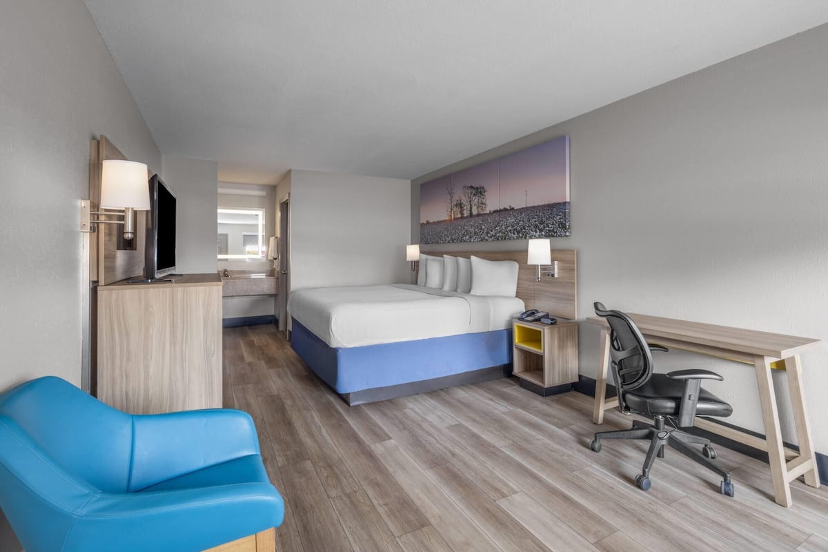 A hotel room with a bed, desk, chair, and a TV.