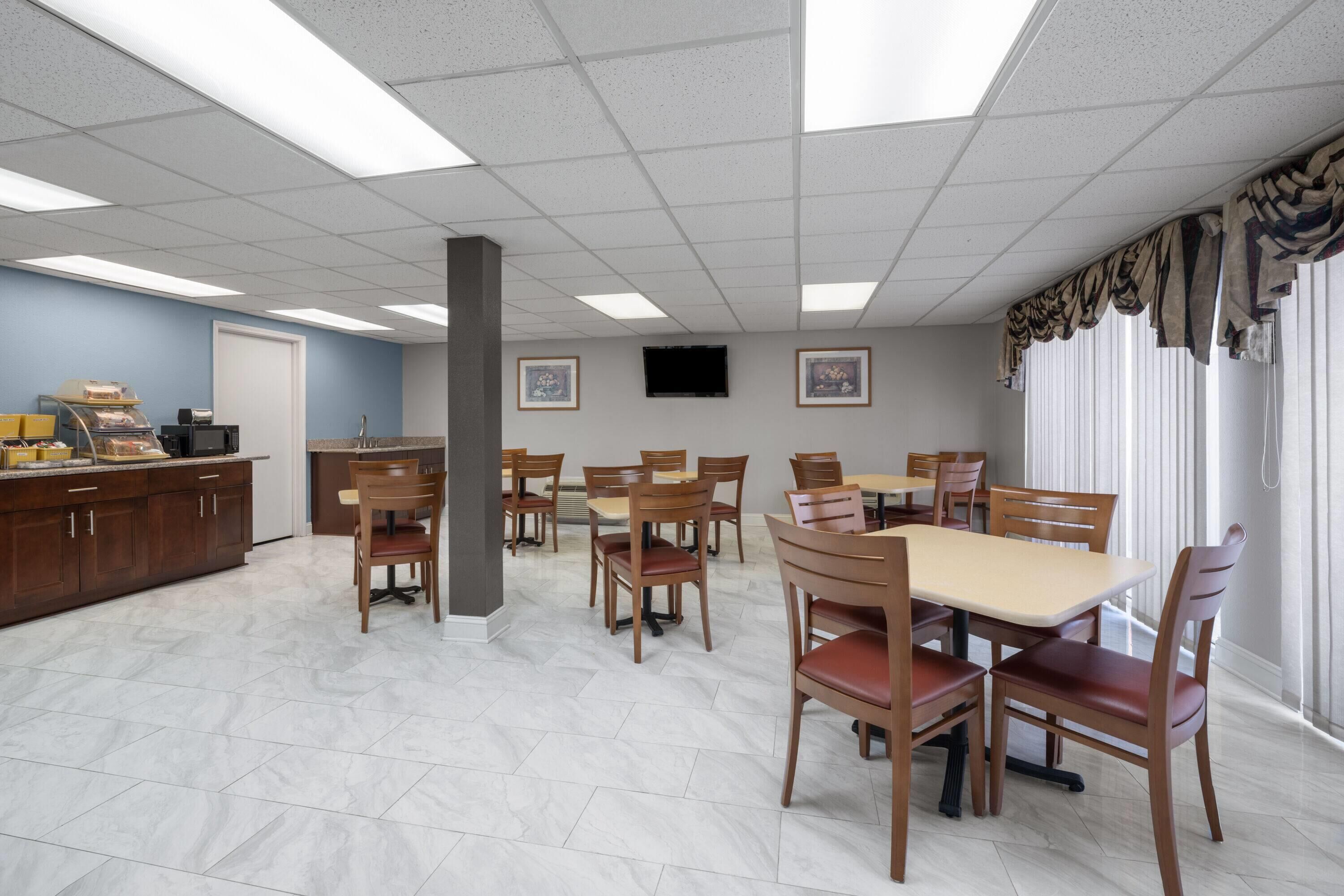 A dining area with multiple tables and chairs, a kitchen area with cabinets and appliances, and a large window with curtains.