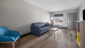 A modern living room with a blue sofa, a wooden coffee table, and a TV stand. - Days Inn by Wyndham Alma (Alma)