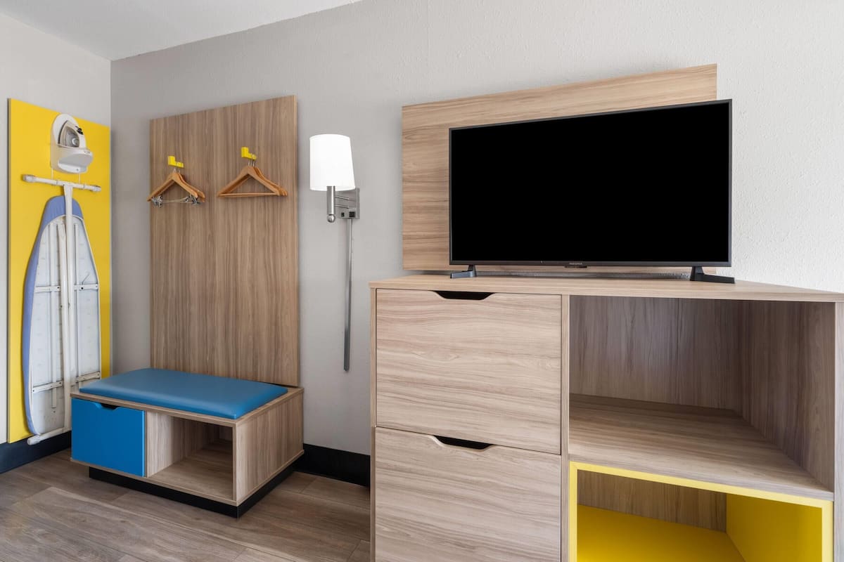 A modern room with a wooden desk, a television, a bench, and a wall-mounted ironing board.