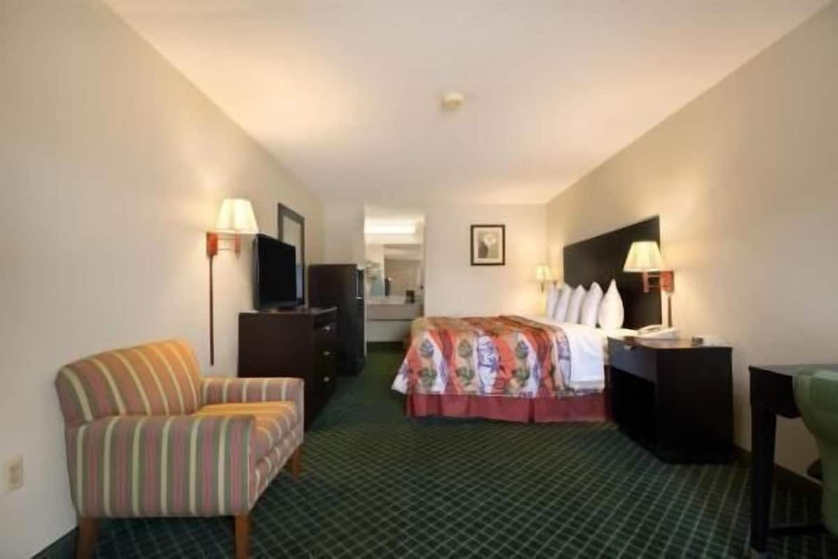 A hotel room with a bed, a chair, a desk, a dresser, and a television.