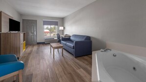 A modern living room with a sofa, a coffee table, a TV, and a bathtub. - Days Inn by Wyndham Alma (Alma)