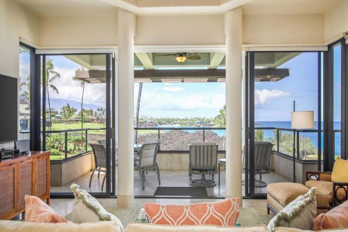 A luxurious living room with a large TV, comfortable seating, and a view of the ocean.