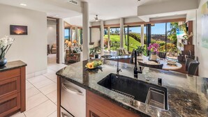 Una cucina moderna con una grande isola, un lavello integrato e vista su un giardino rigoglioso e l'oceano.