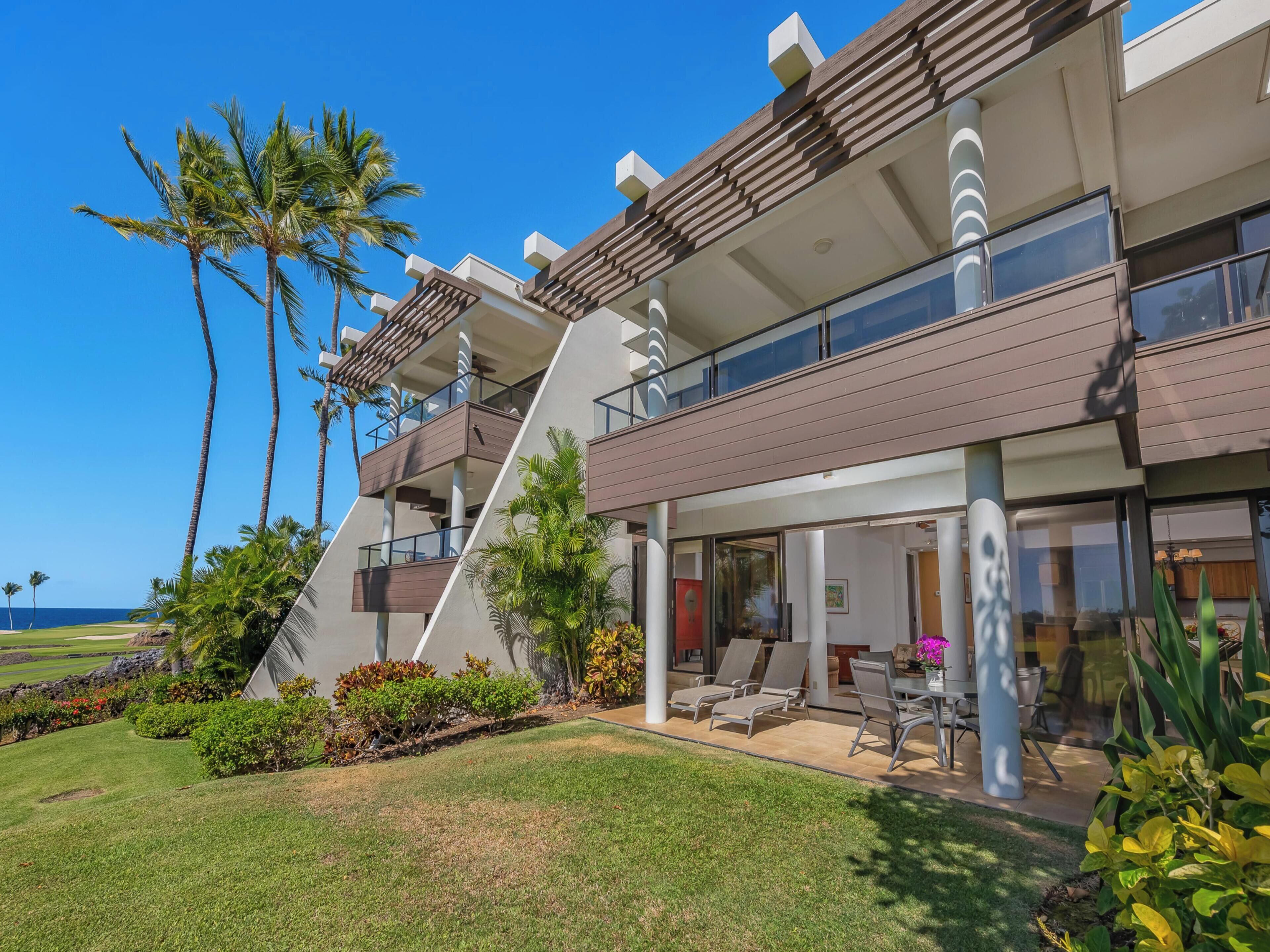 A modern multi-story building with a balcony, a covered outdoor seating area, and a view of the ocean.