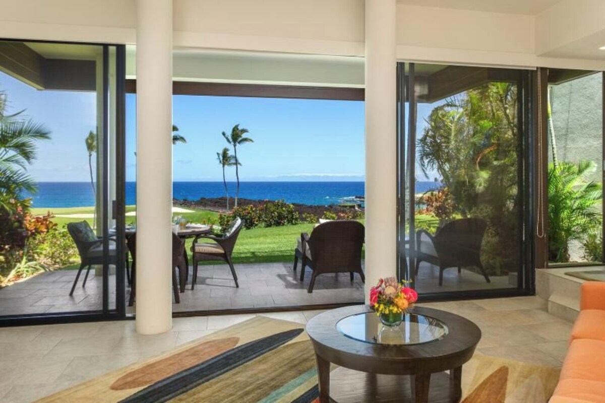 A modern living room with a large glass door leading to a balcony overlooking a scenic ocean view.