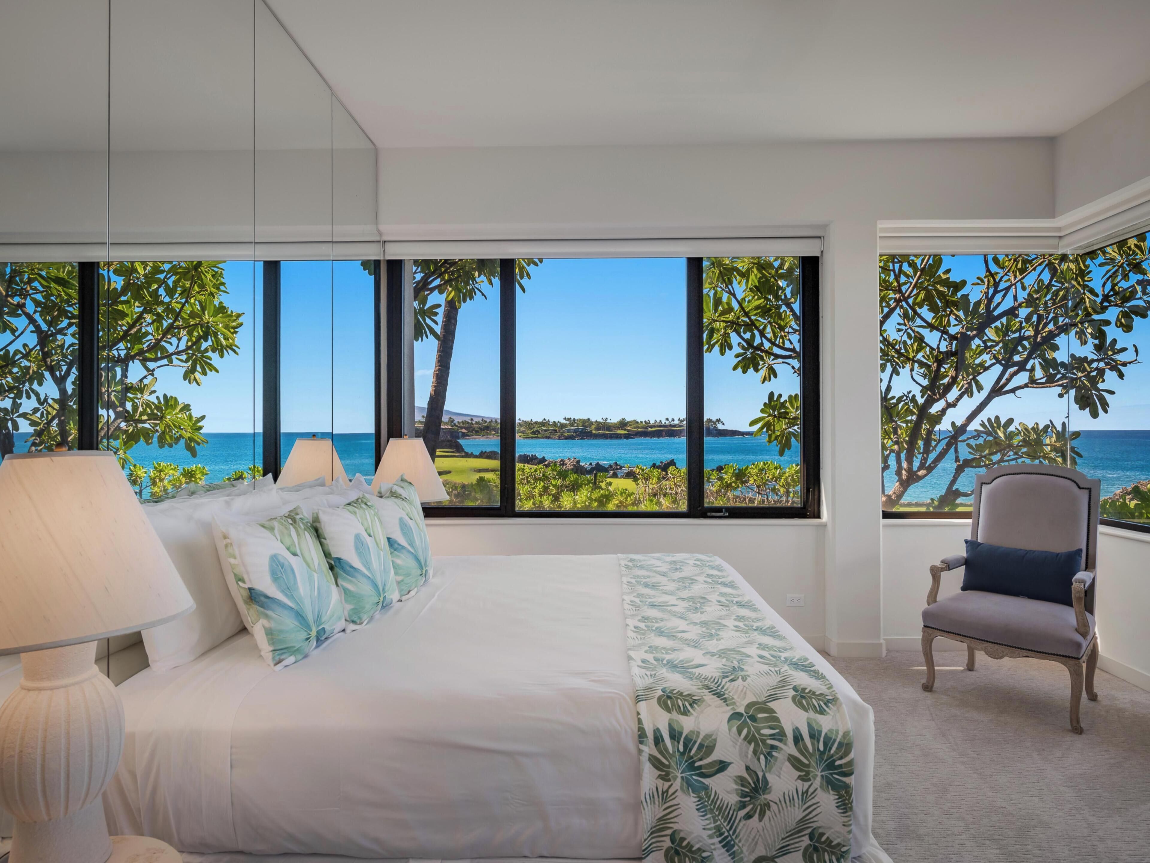 A bedroom with a large window offering a view of the ocean and a chair.