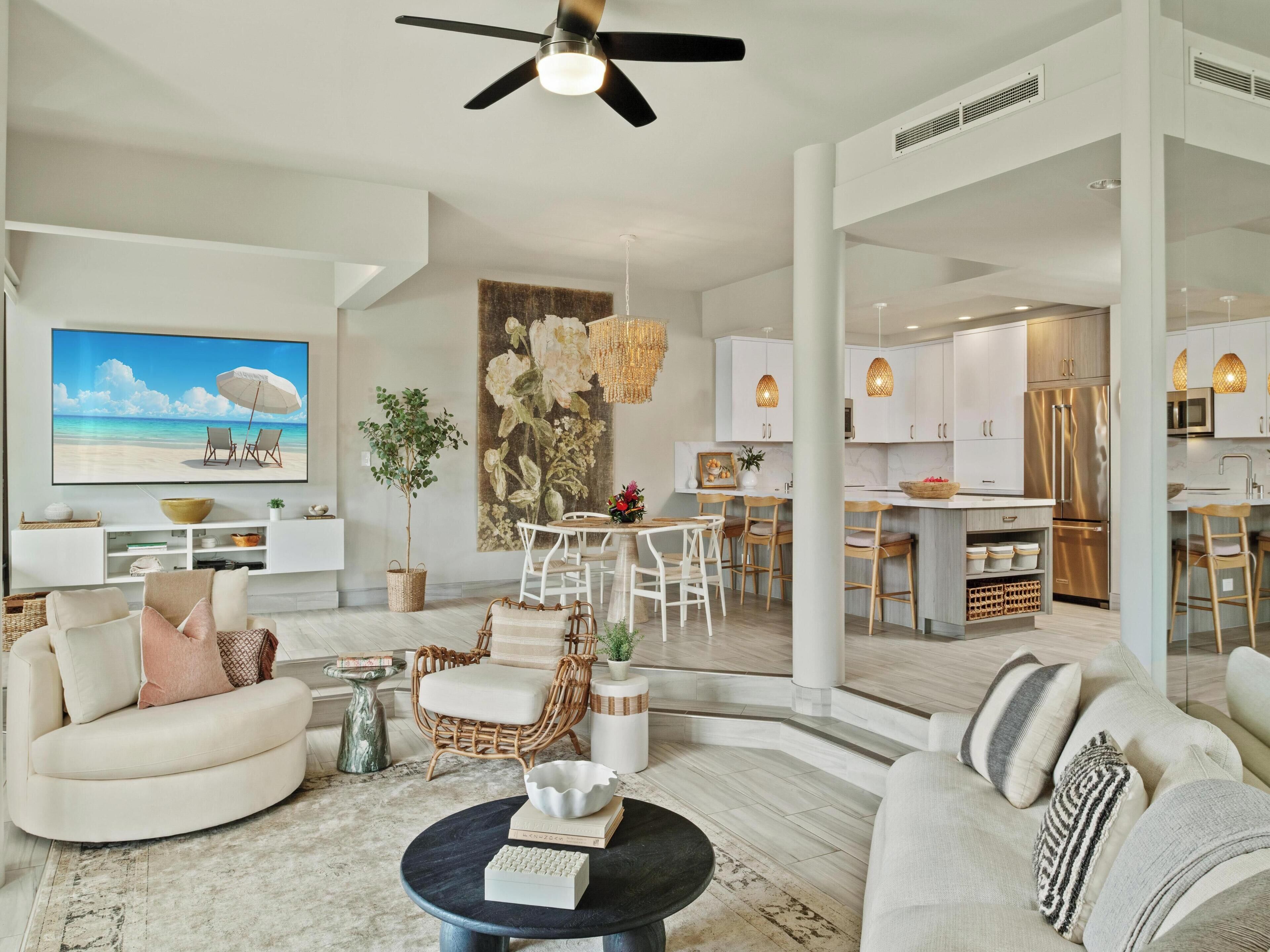A modern living room with a flat-screen TV, comfortable seating, a dining area, and a kitchen.