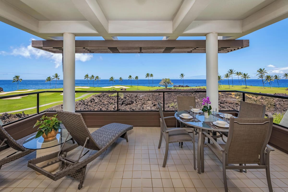 A covered outdoor seating area with a table and chairs, overlooking a golf course and the ocean.